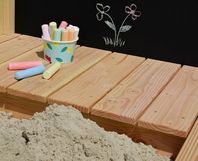 Sandkasten mit einer Tafel und bunten Kreidestücken