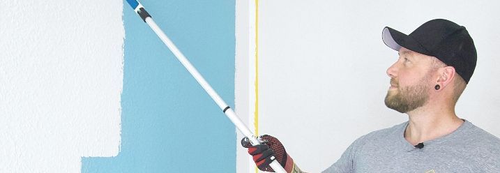 Mann streicht eine Blaue Wand weiß mit einem Roller