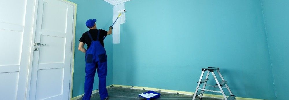 Mann streicht blaue Wand weiß