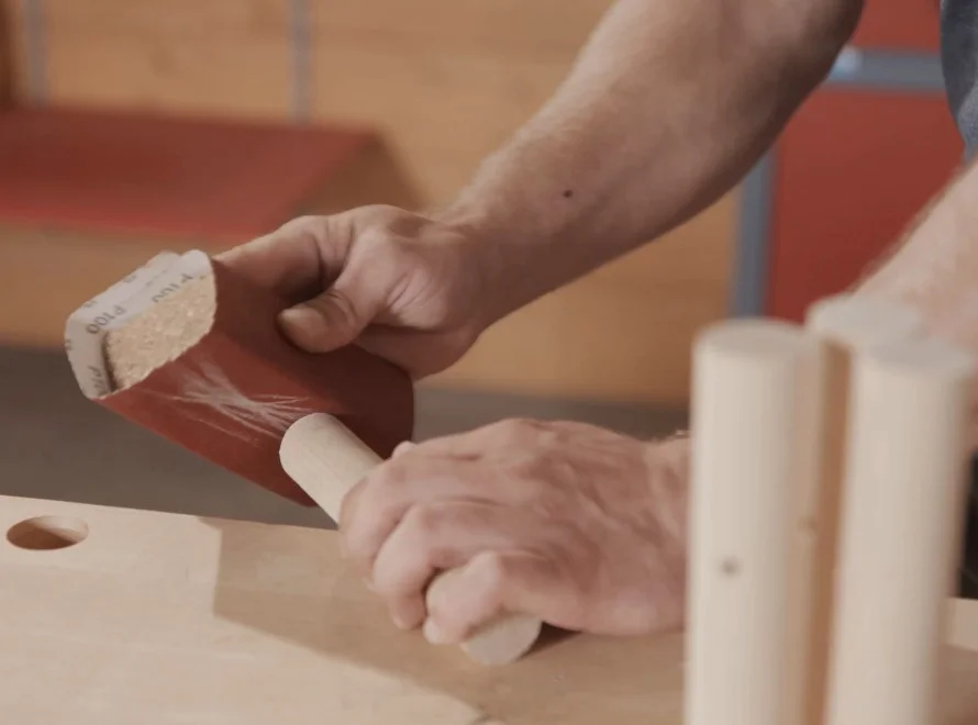 Person schleift Holzstab mit Schleifpapier.