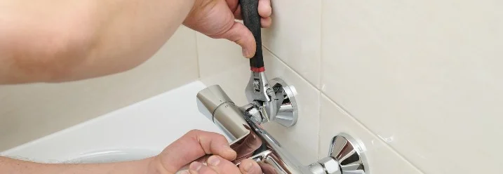 Person montiert Wasserhahn mit Schraubenschlüssel.