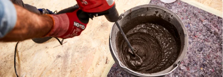 Person mischt mit einem Rührgerät eine Spachtelmasse in einem Eimer
