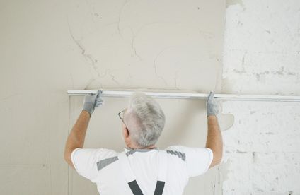 Ein Handwerker zieht Putz mit einer langen Abziehlatte an der Wand ab.