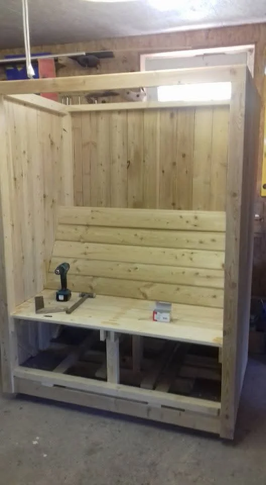 Im Bau befindliche Holzsauna mit Akkuschrauber und Hammer auf der Bank.