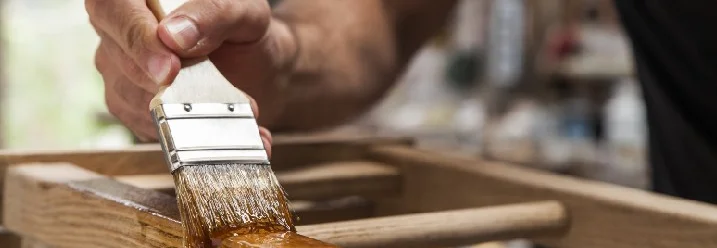 Person lackiert Holz mit Pinsel