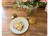 Ein belegtes Brot mit Avocado, ein Glas Saft und Blumen.