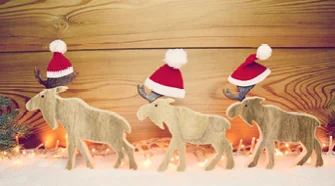 Zwei Holz-Elche mit Weihnachtsmützen im Schnee