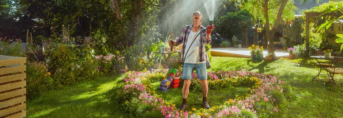 Mensch bewässert ein Blumenbeet mit einer Schlauchbrause und freut sich.