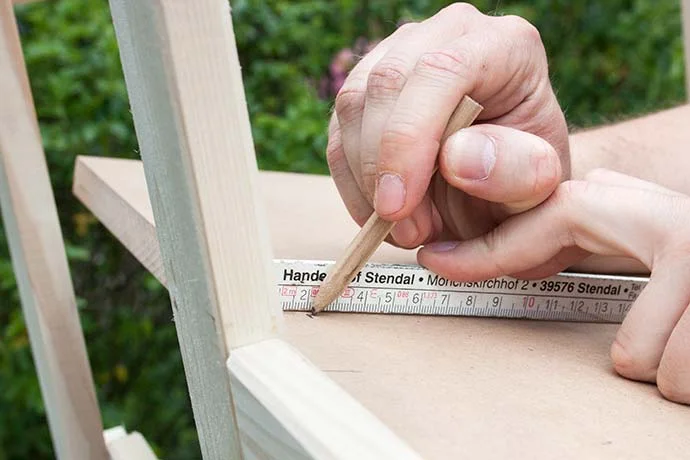 Person zeichnet mit Bleistift eine Markierung auf ein Holzbrett