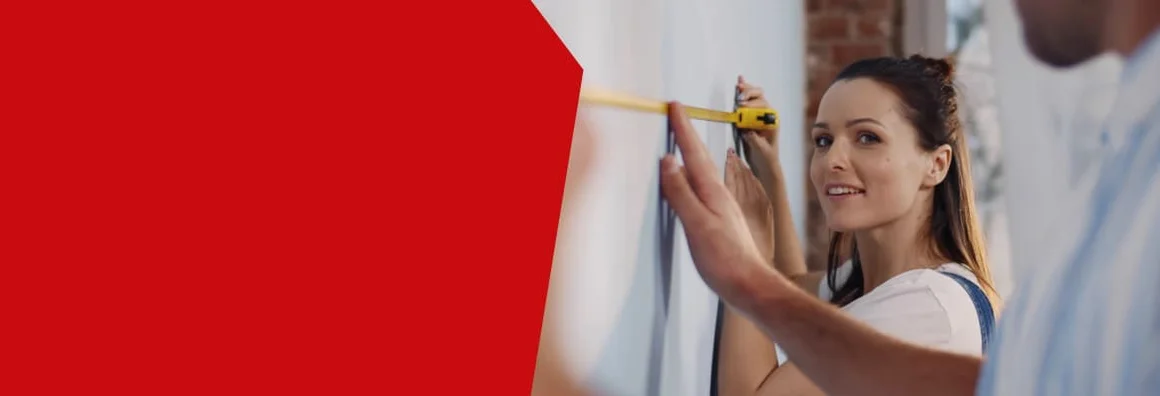 Zwei Personen messen eine Wand mit einem Maßband aus.