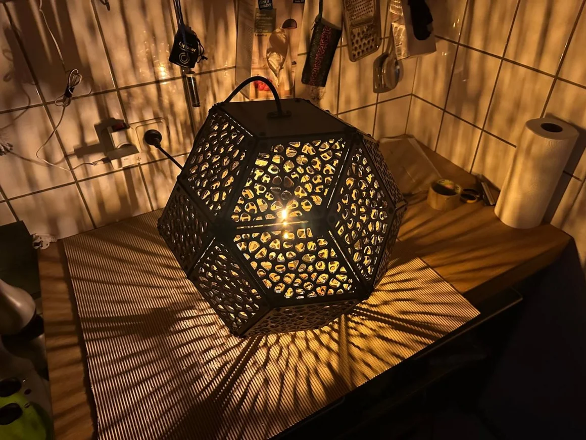 Eine geometrische Lampe mit durchbrochenem Muster wirft Schatten auf eine Arbeitsplatte.