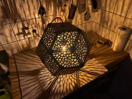 Eine geometrische Lampe mit durchbrochenem Muster wirft Schatten auf eine Arbeitsplatte.