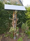 Eine große Vogelfutterstation aus Holz und Metall in einem Garten.