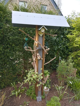 Eine große Vogelfutterstation aus Holz und Metall in einem Garten.