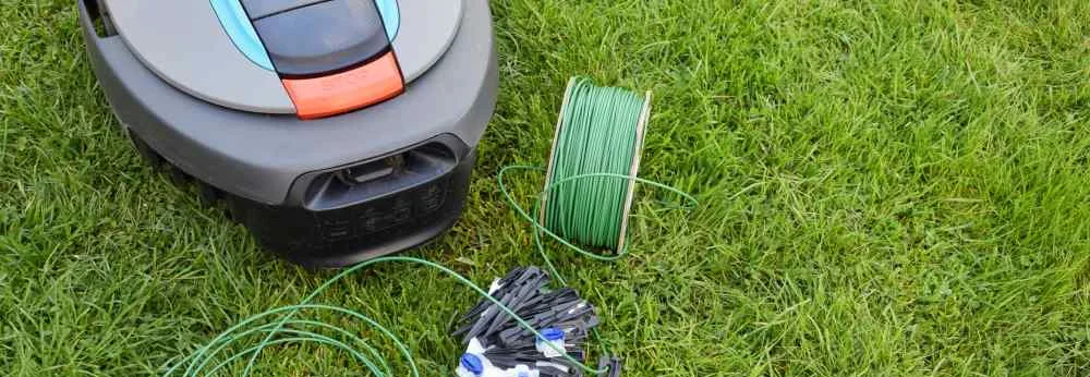 Mähroboter mit Installationszubehör wie Begrenzungskabel und Haken auf einem Rasen.