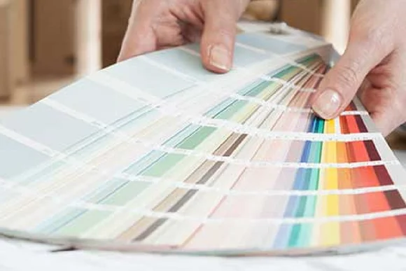 Hände halten einen Fächer mit Farbmustern.