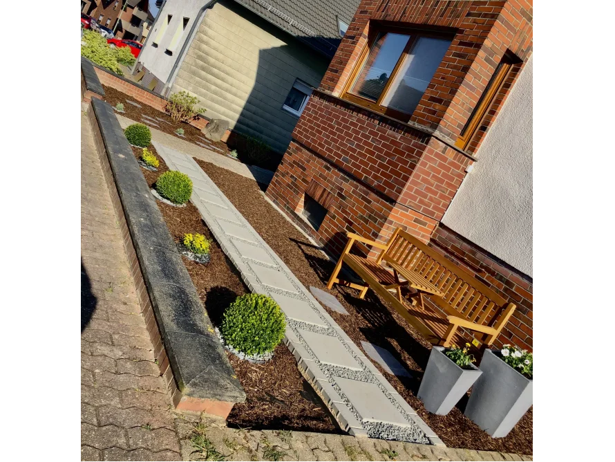 Gepflasterter Weg in einem Vorgarten mit Holzbank