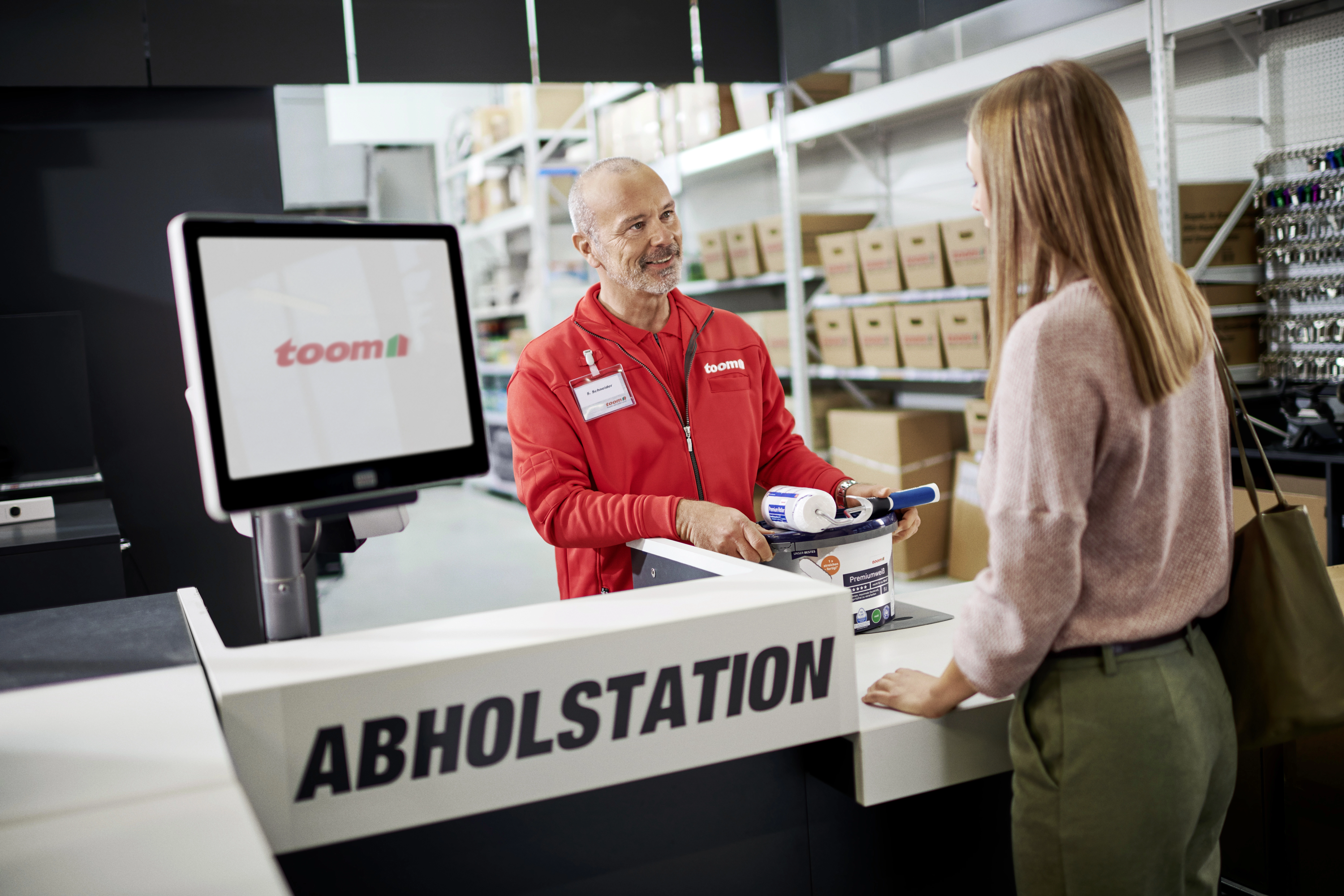 Eine Person erhält einen Farbeimer und eine Farbrolle an einer Abholstation.