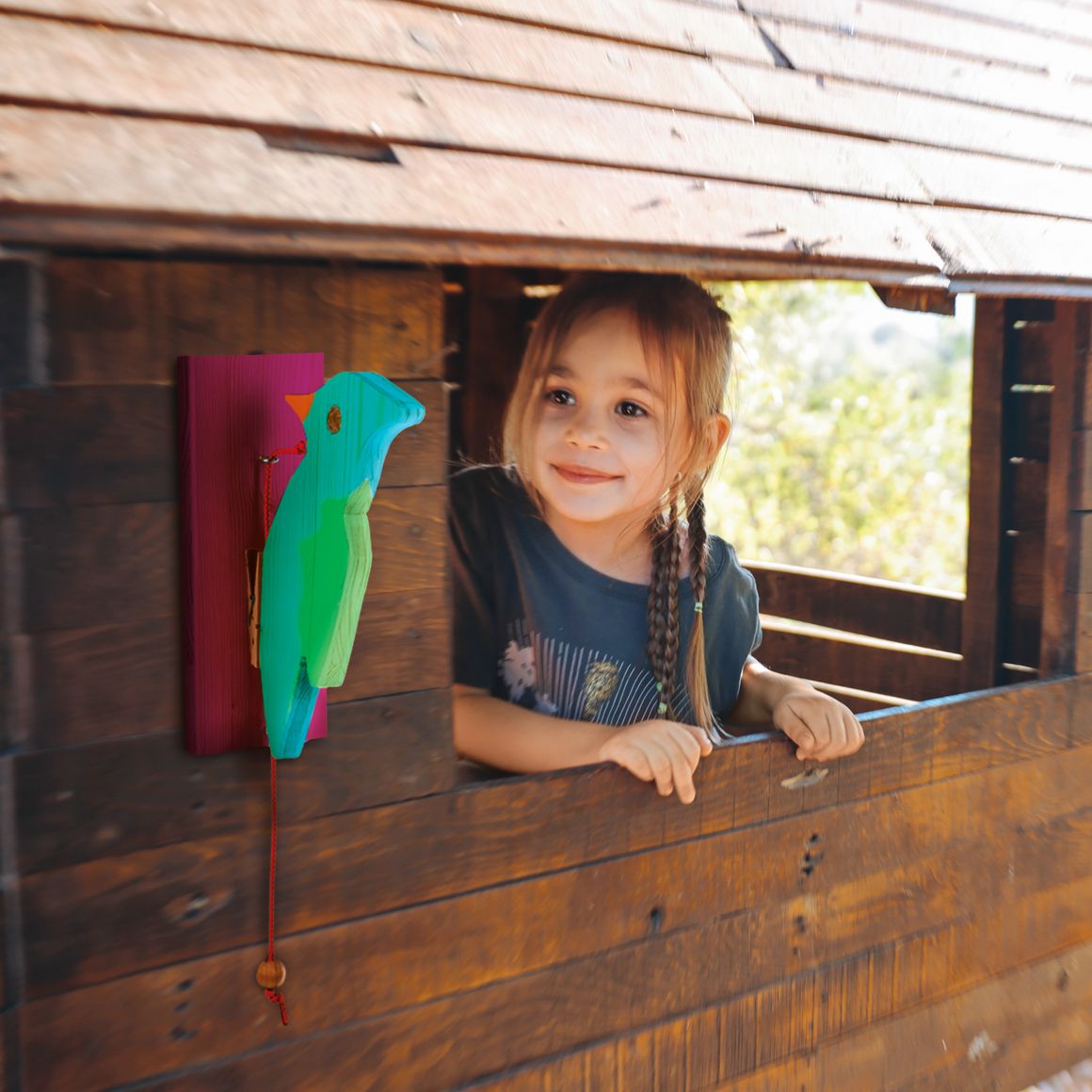 Kind in einem Spielhaus aus Holz mit buntem Holzvogel.