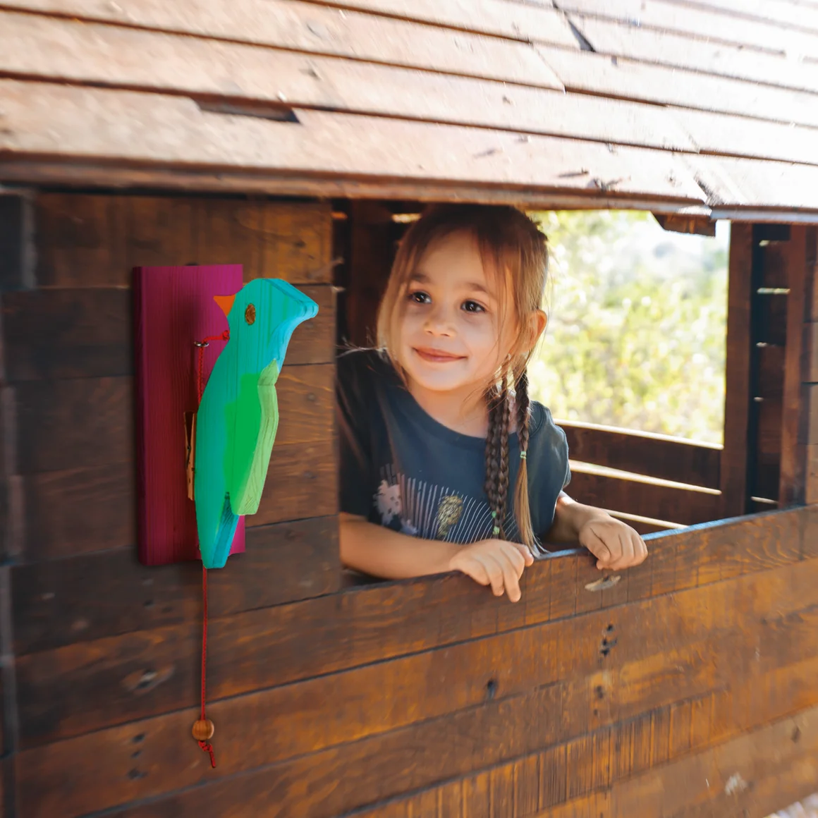 Kind in einem Spielhaus aus Holz mit buntem Holzvogel.