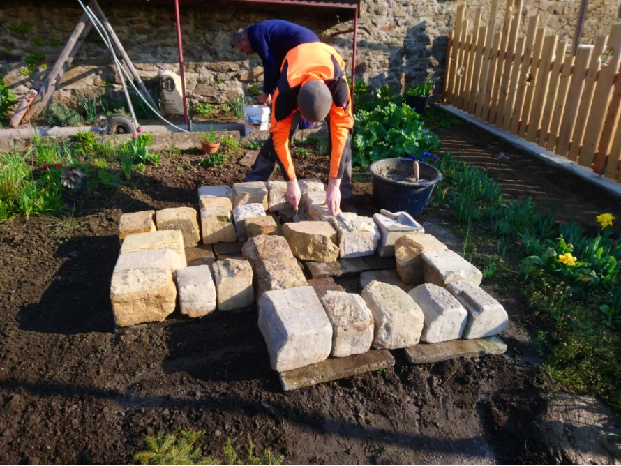 Person baut Mauer aus Sandsteinen