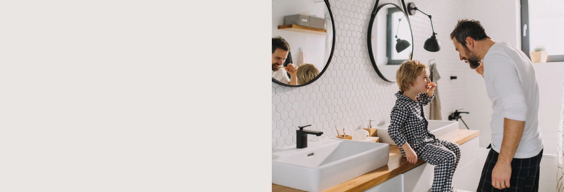 Mann steht vor Kind, welches auf Waschtisch im Bad sitzt