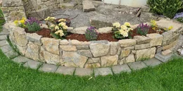 Eine geschwungene Trockenmauer als Hochbeet mit Blumenbepflanzung.