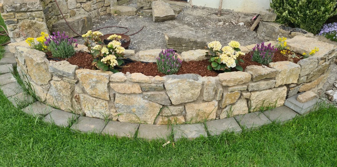 Eine geschwungene Trockenmauer als Hochbeet mit Blumenbepflanzung.
