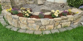 Eine geschwungene Trockenmauer als Hochbeet mit Blumenbepflanzung.