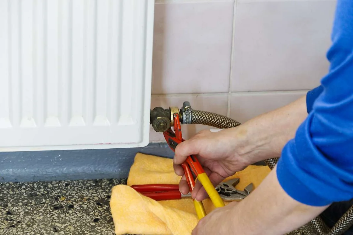 Eine Person arbeitet mit einer Rohrzange an einem Heizkörper.