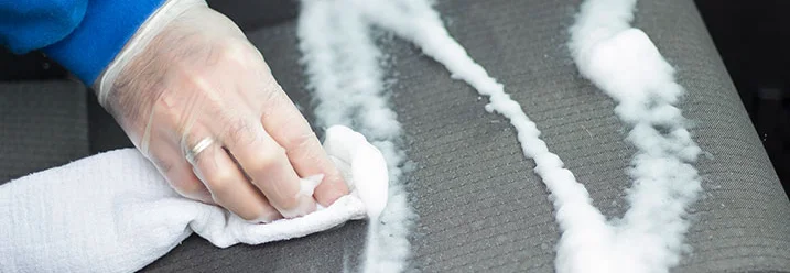 Hand reinigt Autositz mit Tuch