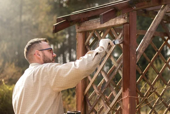 Person streicht Gartenlaube mit Pinsel