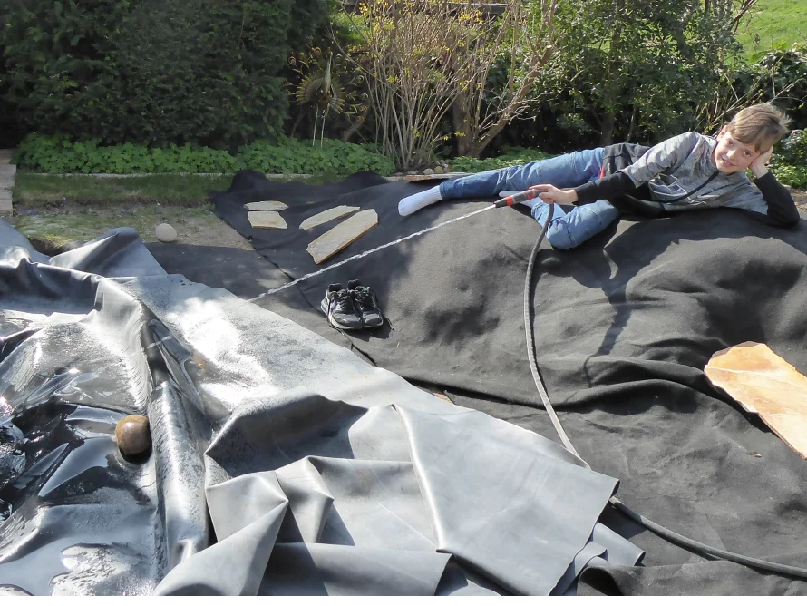 Kind spritzt mit Gartenschlauch Wasser auf Plane