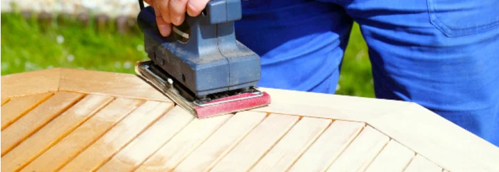 Person schleift Holztisch mit Schleifmaschine