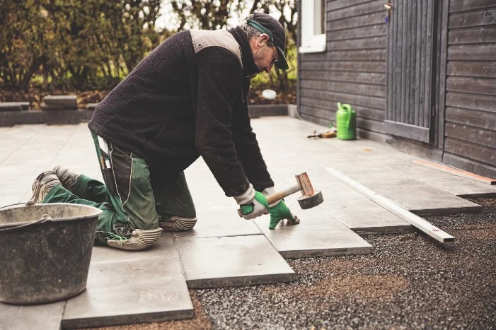 Person verlegt Terrassenplatten mit Gummihammer