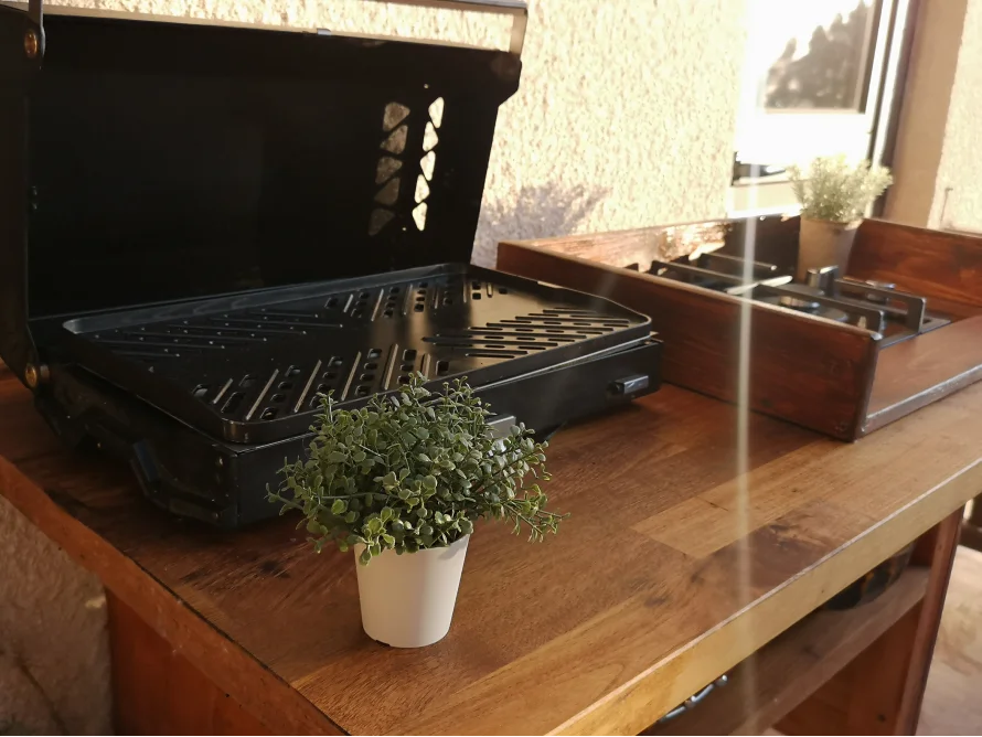 Ein geöffneter Grill und ein Gaskocher auf einem Holztisch.
