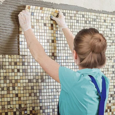 Person bringt Mosaikfliesen an Wand an