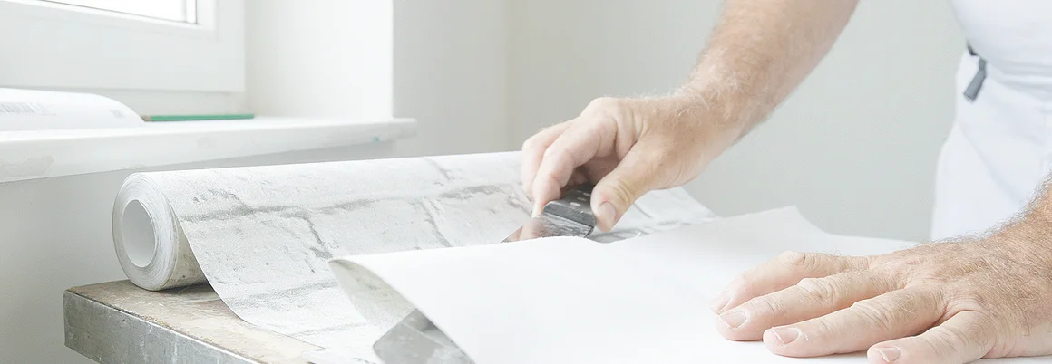 Person schneidet Tapete mit Cuttermesser