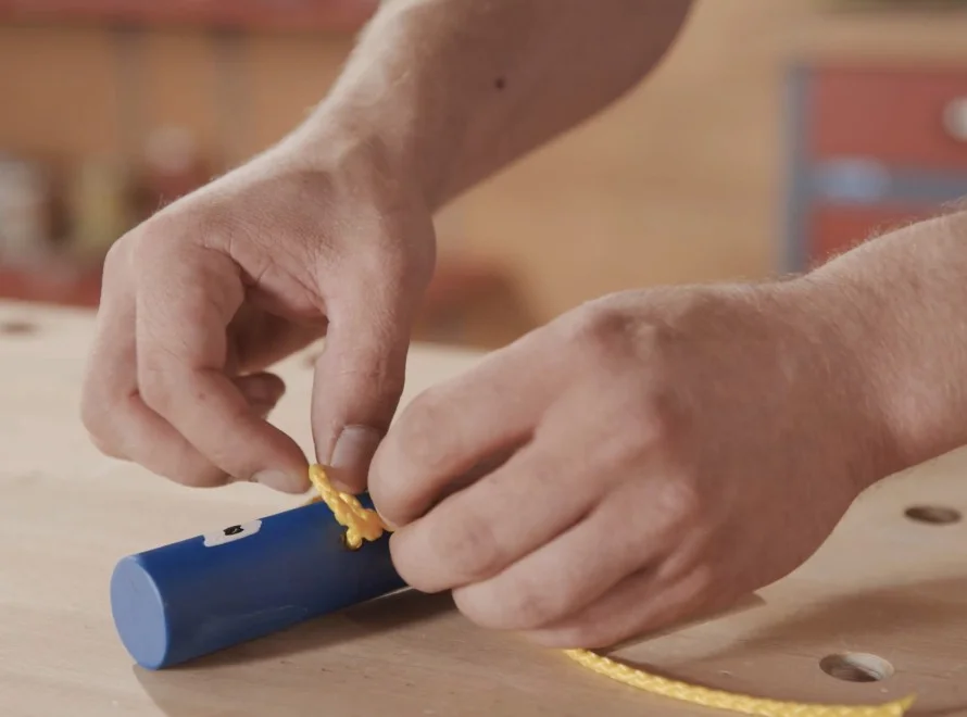 Hände fädeln Seil durch Loch in blauem Holz