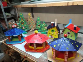 Bunte, handgefertigte Vogelhäuschen, Futterkrippen und Weihnachtsbäume aus Holz auf einer Werkbank.
