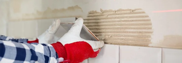 Person bringt Fliesen an einer Wand an