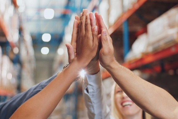 Gruppe von Menschen gibt sich ein High-Five in einer Lagerhalle.