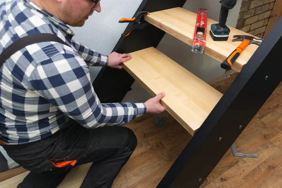 Person montiert Holzstufe an einer Treppe.