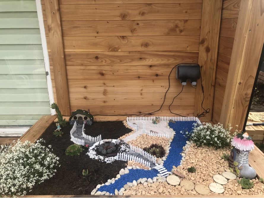 Ein Feengarten mit Miniaturhaus und blauem Bach.