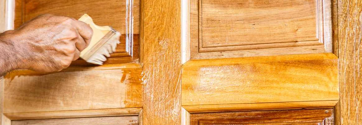 Person lasiert eine Tür mit einem Pinsel.