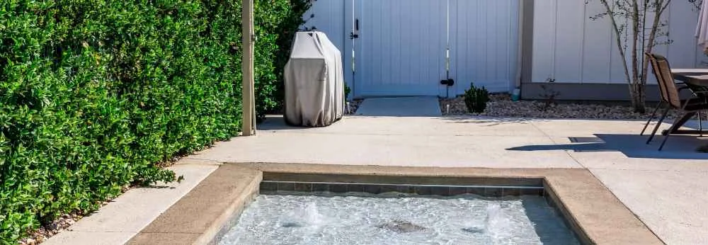 Ein kleiner Pool auf einer Terrasse neben einer hohen, grünen Hecke.
