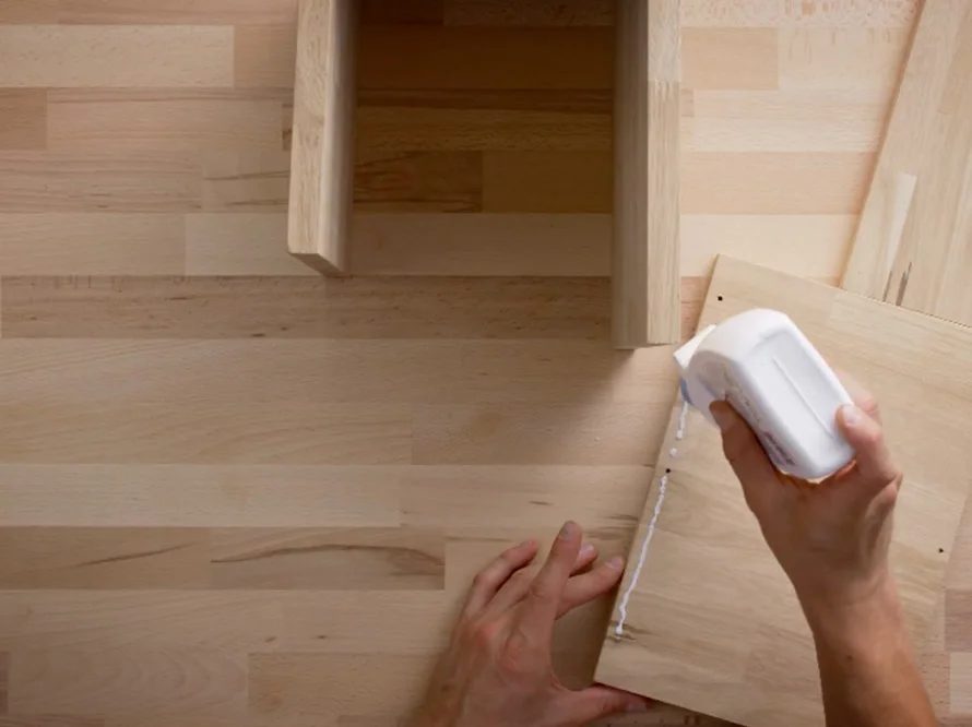 Person klebt Holzbrett mit Kleber zusammen