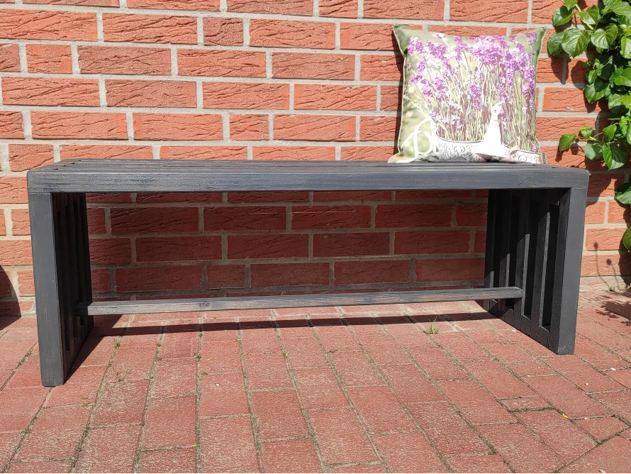 Schwarze Holzbank vor Backsteinmauer