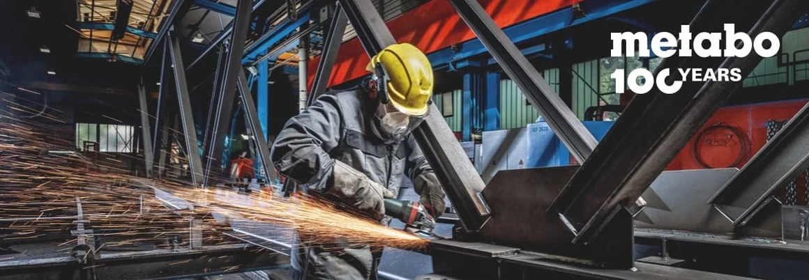 Person mit Winkelschleifer an Metallträger