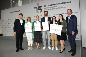 Pressefoto Berlin/ Juri Reetz Sechs Personen posieren mit Zertifikaten und einem Mann im Anzug